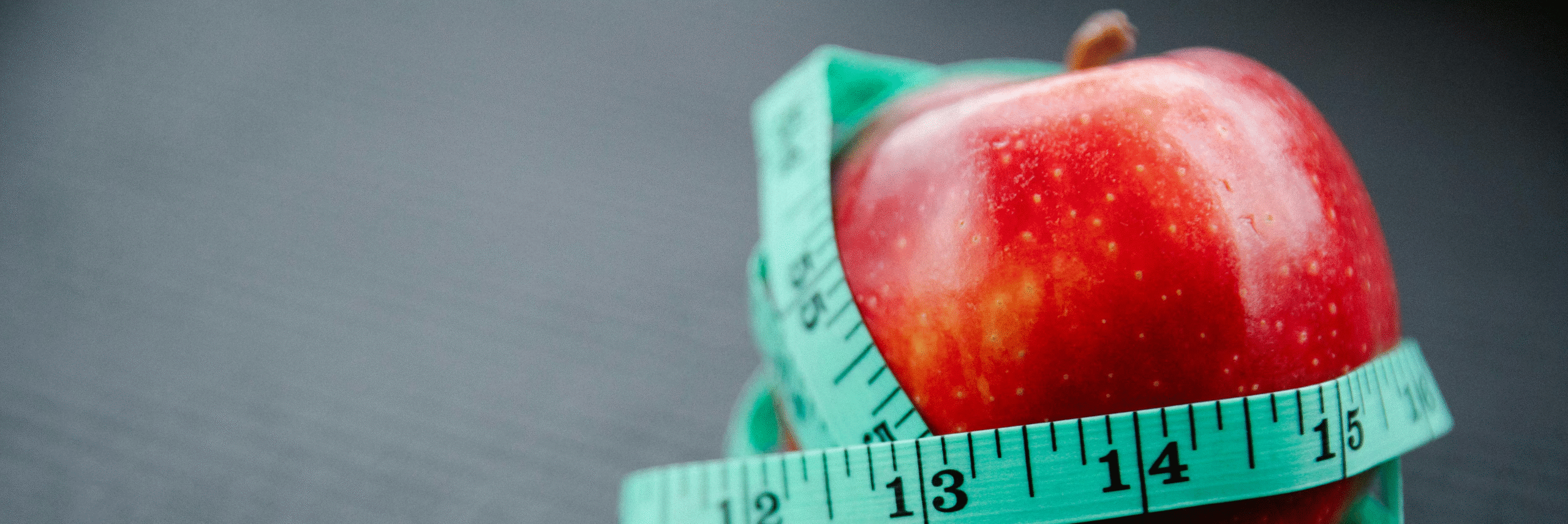 Red apple wrapped with a teal measuring tape, symbolizing healthy weight loss and calorie tracking