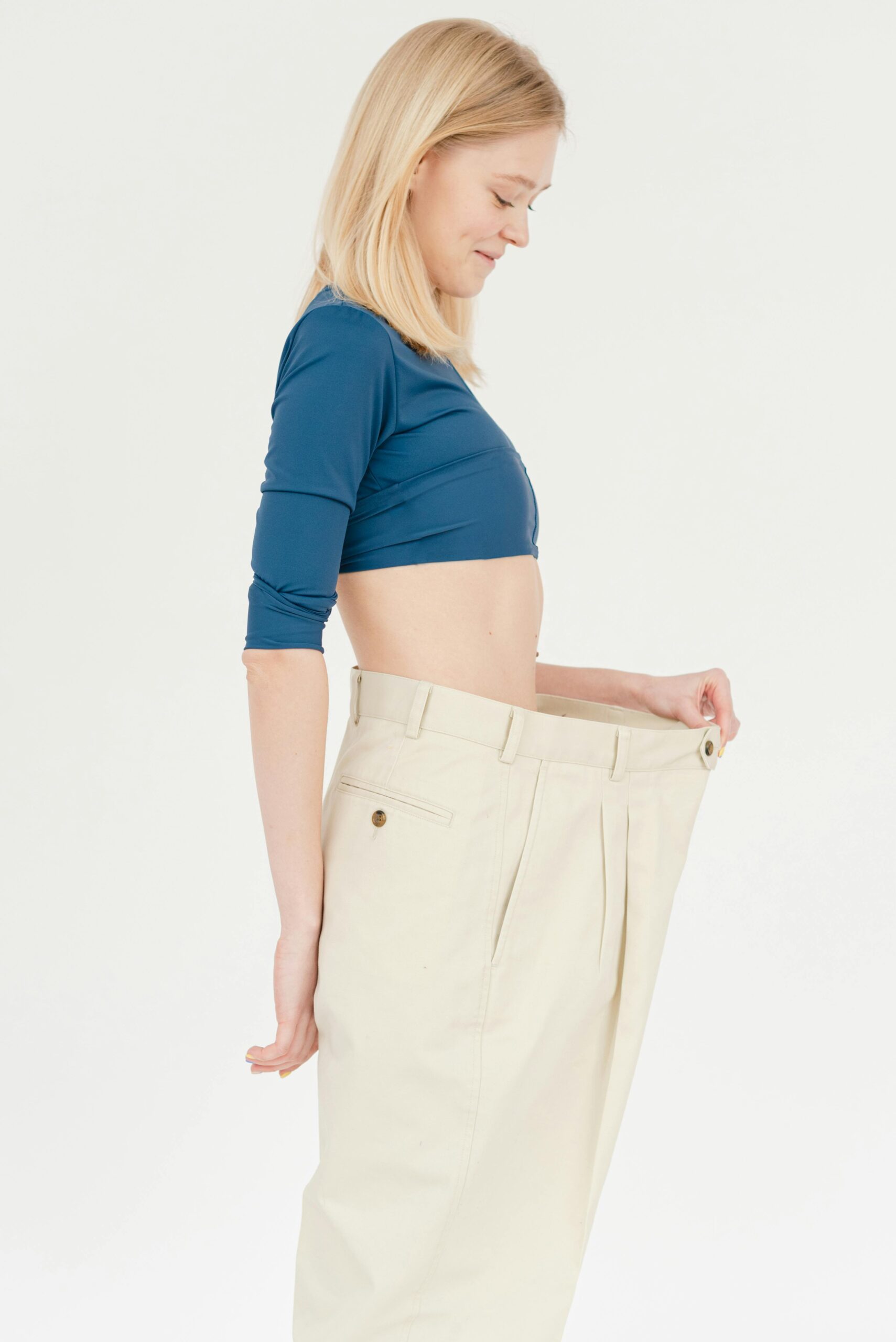 Woman smiling and holding out the waistband of oversized pants to show her weight loss progress.