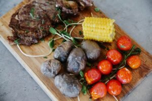 Grilled steak with roasted potatoes, cherry tomatoes, and corn on the cob served on a plate.